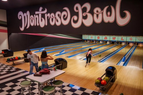 A vibrant bowling alley with colorful lanes, featuring two people chatting and one person bowling.