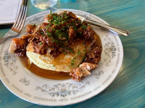 A plate of fluffy pancakes topped with savory meat, drizzled in sauce, and garnished with chopped chives.