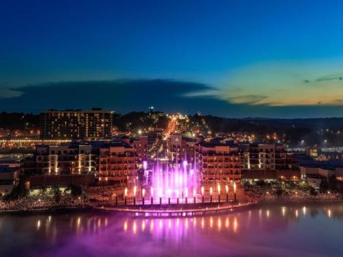 Colorful fountains illuminated at dusk, with a vibrant waterfront and city skyline in the background.
