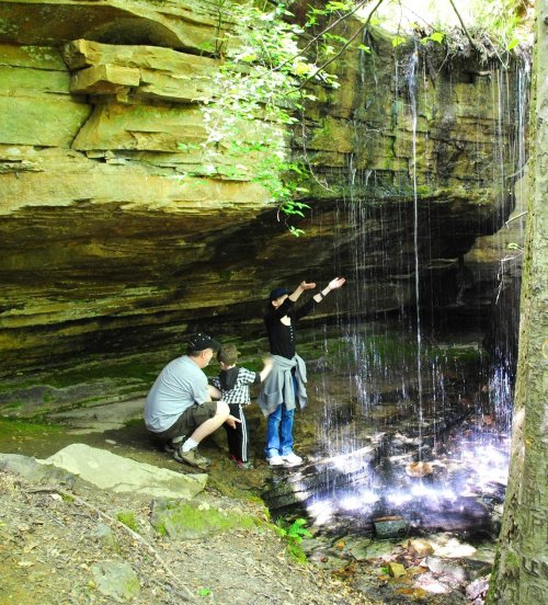 A family stands near a small waterfall in a rocky area, with one person reaching out towards the water.