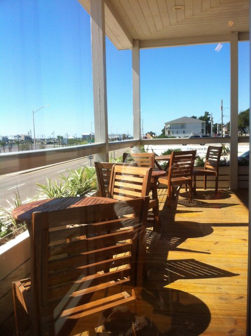 A sunny outdoor patio with wooden tables and chairs, overlooking a street and clear blue sky.