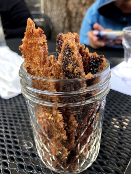A glass jar filled with crispy, golden-brown snacks, sitting on a table with a blurred background.
