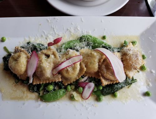A plate of ravioli on a bed of spinach, garnished with radishes and peas, topped with grated cheese.