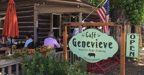 A rustic café sign reading "Cafe Genevieve" with outdoor seating, flowers, and an American flag in the background.