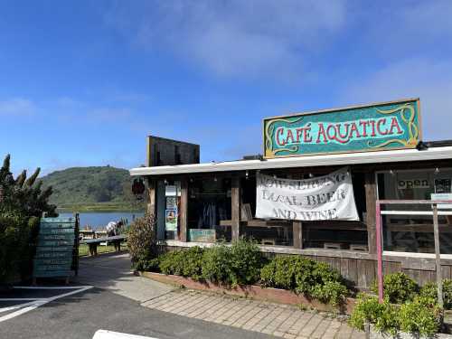 A rustic café named "Cafe Aquatica" with a sign advertising local beer and wine, surrounded by greenery and a scenic view.