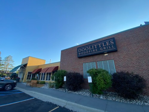 Exterior of Doolittle's Woodfire Grill, featuring a brick facade and outdoor seating area. Clear blue sky in the background.