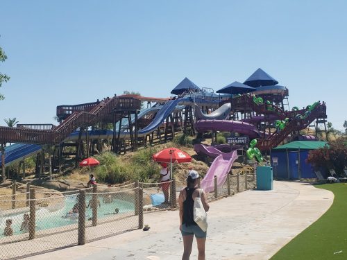 A water park with colorful slides, people enjoying the pool, and shaded areas under umbrellas on a sunny day.