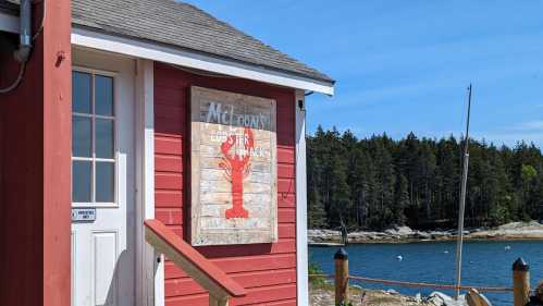 A red building with a sign reading "McLoon's Lobster Shack" near a calm waterfront and trees in the background.