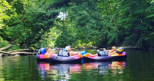Two people relax on colorful inner tubes in a serene, tree-lined river.