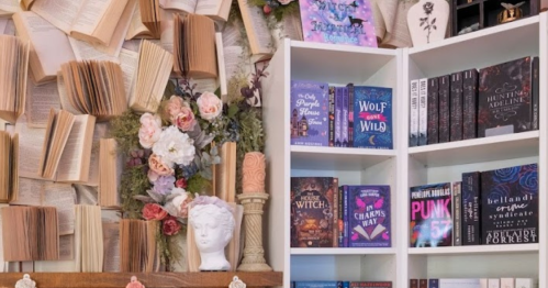 A cozy book display with open books on the wall, a floral arrangement, and a white bookshelf filled with various titles.