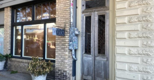 A weathered building entrance with double doors, a sign reading "Thanks," and potted plants by the window.