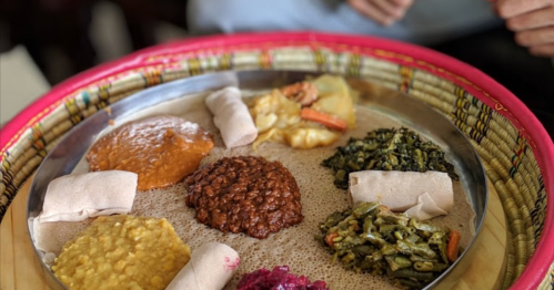 A colorful platter of Ethiopian food featuring various stews, vegetables, and injera on a woven basket.