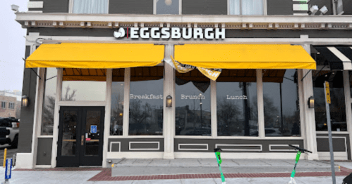 Exterior of Eggsburgh restaurant with yellow awnings, featuring windows displaying "Breakfast, Brunch, Lunch" signage.