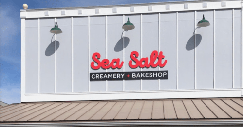 Sign for "Sea Salt Creamery + Bakeshop" on a white building with green light fixtures.
