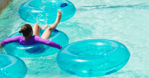 A person in a purple swimsuit enjoys a water slide, sitting on a blue inner tube in a pool.
