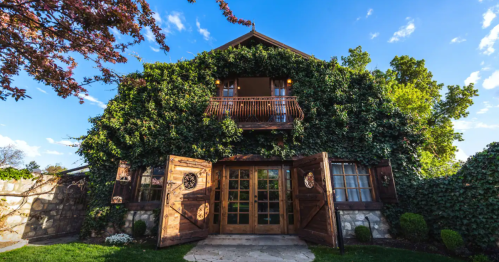A charming ivy-covered house with wooden double doors and a balcony, set against a clear blue sky.