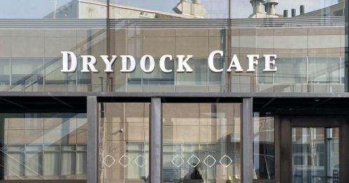 Sign for "Drydock Cafe" displayed on a modern building with reflections in the glass.