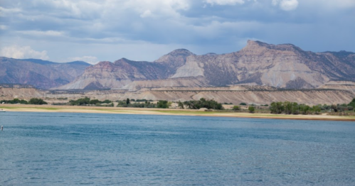 A serene landscape featuring a calm river with mountains in the background under a partly cloudy sky.