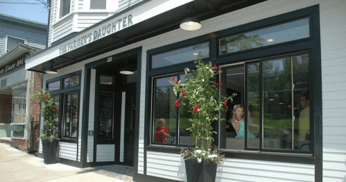 Exterior of "The Farmer's Daughter" restaurant, featuring large windows, flower planters, and a welcoming atmosphere.