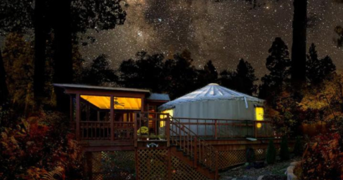 A cozy yurt and wooden deck under a starry night sky, surrounded by trees and autumn foliage.