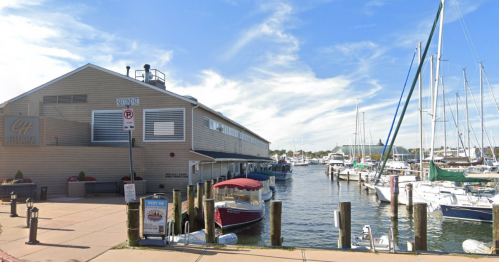 A marina with boats docked, a waterfront building, and a clear blue sky in the background.