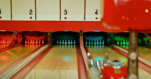A bowling alley with illuminated lanes and colorful lights, showing pins ready to be knocked down.