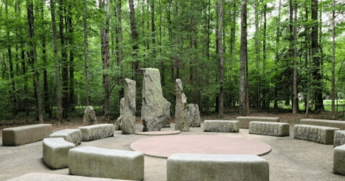 A circular stone arrangement in a forested area, surrounded by tall green trees.