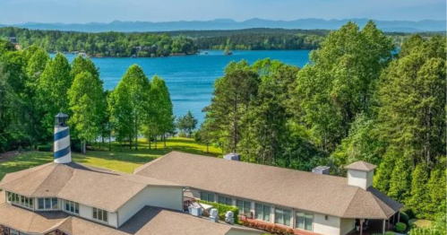 Aerial view of a lakeside property with a lighthouse, surrounded by lush trees and mountains in the background.