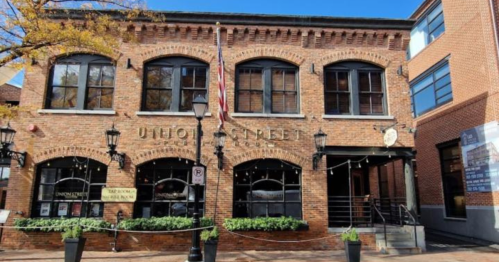 Historic brick building with large windows, outdoor seating, and an American flag, located on Union Street.