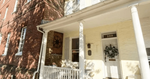 A charming porch with white railings, a wreath on the door, and brick buildings in the background.