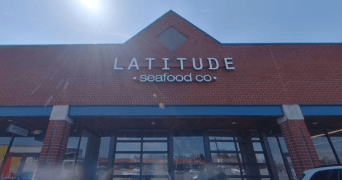 Exterior of a brick building with a sign that reads "LATITUDE seafood co" against a clear blue sky.