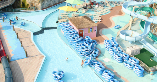 Aerial view of a water park with blue slides, a lazy river, and numerous inflatable tubes scattered around.