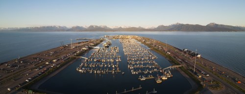 Aerial view of a marina filled with boats, surrounded by mountains and water under a clear sky.