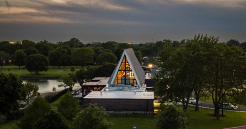 Aerial view of a modern triangular building surrounded by trees and a park at dusk.