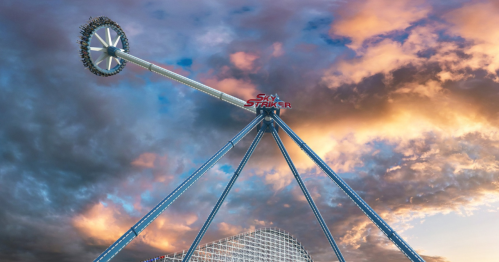 A tall amusement park ride with a circular top, set against a dramatic sunset sky.