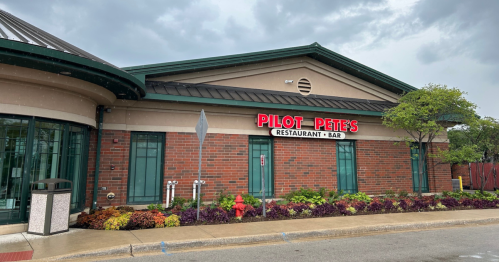 Exterior of Pilot Pete's Restaurant & Bar, featuring a brick facade and colorful landscaping under a cloudy sky.