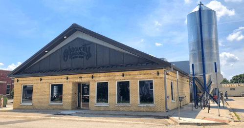 Exterior of Obscurity Brewing Company, featuring a brick building and a large silver brewing tank beside it.