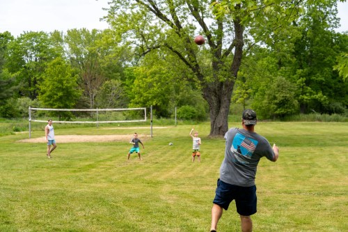 A man throws a football to two kids playing in a grassy field with a volleyball net in the background.