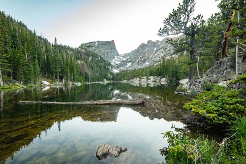 A serene mountain lake surrounded by lush trees and rocky peaks, reflecting the landscape in calm waters.