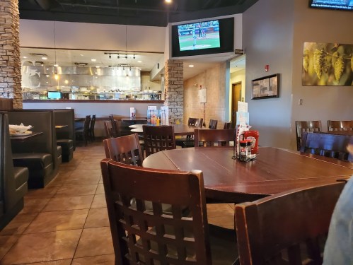 Interior of a restaurant featuring wooden tables, booths, and a TV showing a sports game in the background.