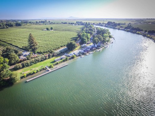 Aerial view of a serene river surrounded by lush greenery and vineyards, with boats docked along the shore.