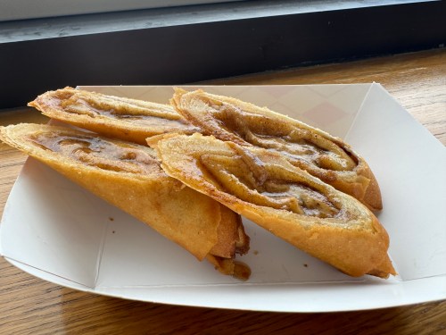 Three golden-brown, crispy pastries filled with a swirled cinnamon and sugar mixture, served in a paper tray.