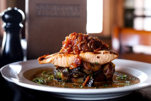 Grilled salmon fillet topped with a savory sauce, served on a bed of roasted vegetables and herbs.