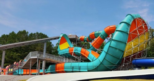 Colorful water slides twist and turn at a water park, surrounded by greenery and a clear blue sky.