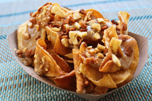 A close-up of a serving of crispy potato chips topped with caramel and chopped nuts in a paper tray.