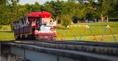 A colorful miniature train on tracks in a park, surrounded by green grass and trees.