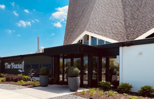 Modern building entrance with large glass doors, planters, and a sign reading "The Portal on the Lake" against a blue sky.