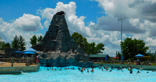 A water park scene featuring a large rock formation and a pool filled with people enjoying the sunny day.
