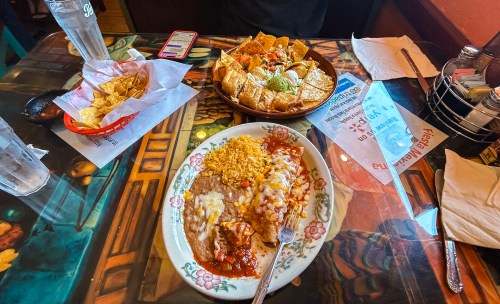 A table with a plate of enchiladas and rice, a bowl of nachos, and a basket of tortilla chips.