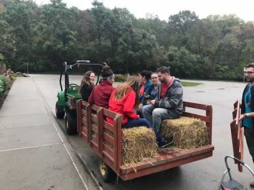 A group of people sitting on a hayride trailer, enjoying a ride through a wooded area on a cloudy day.